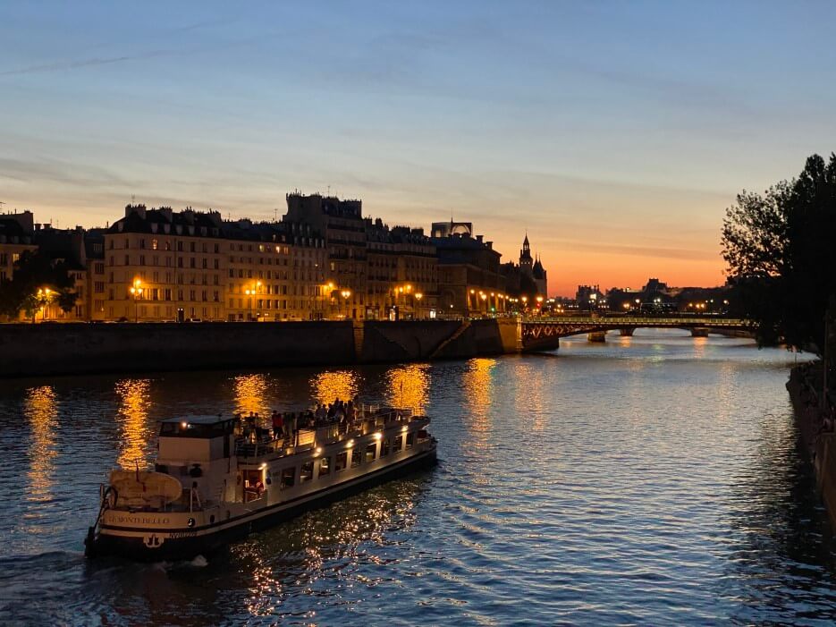 Stuning photo of the Seine at sunset with the lights from a boat and a building reflecting on the water