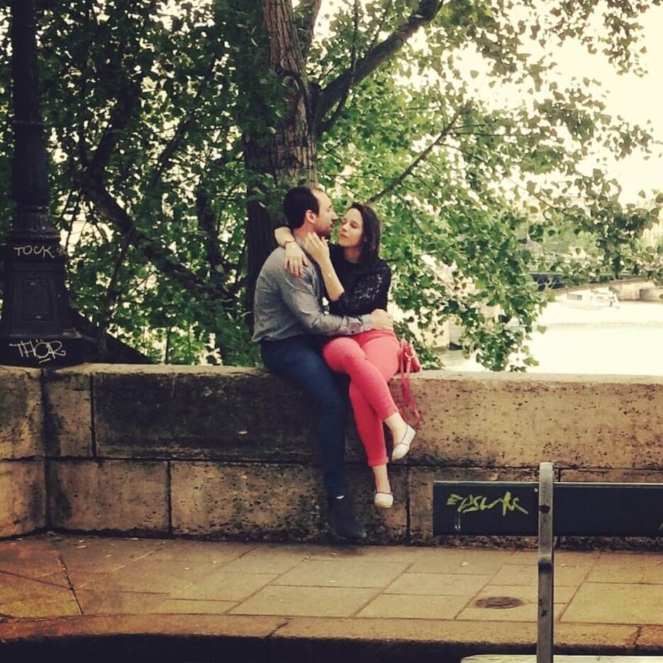 A couple lovingly embracing on a wall along the Seine in Paris