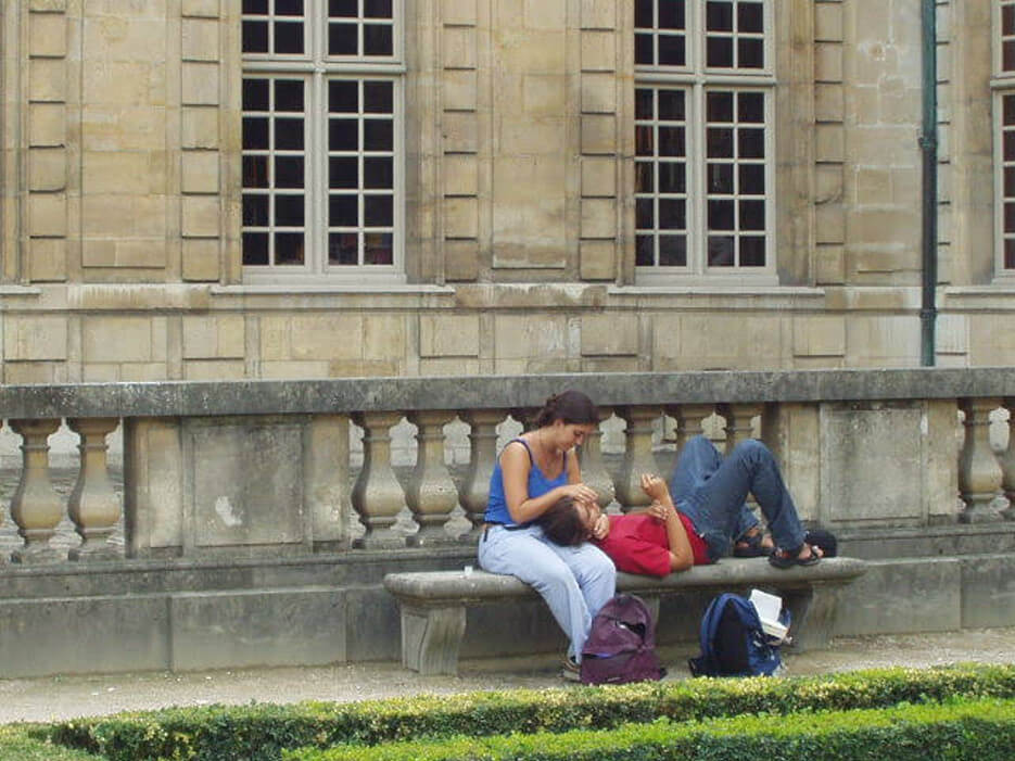 A couple lounging on a bench in Paris, him with his head in her lap
