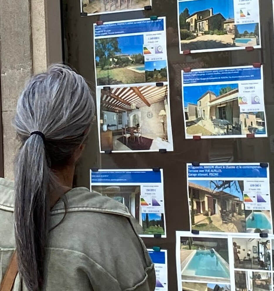 A woman looking at the real estate listing in the window of a real estate office in France