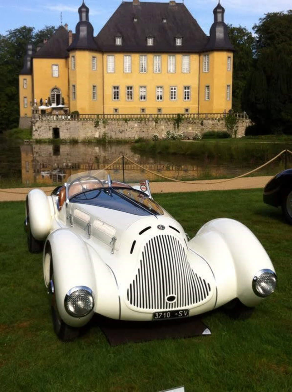 An antique sports car parked in front of a French chateau