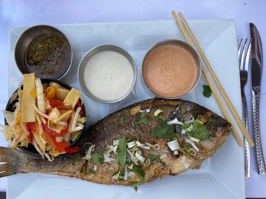 Photo of a dinner plad with a whole fried fish and sauces