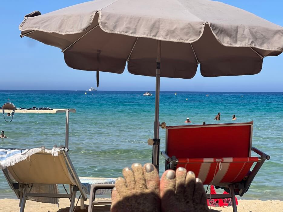 Adrian Leeds' sandy toes resting on the beach in Corsica