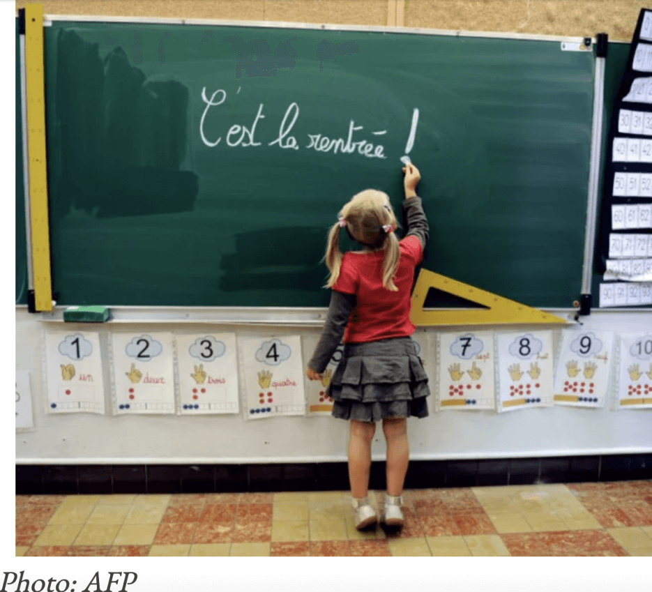 A little girl at a school blackboard writing out La Rentree in French