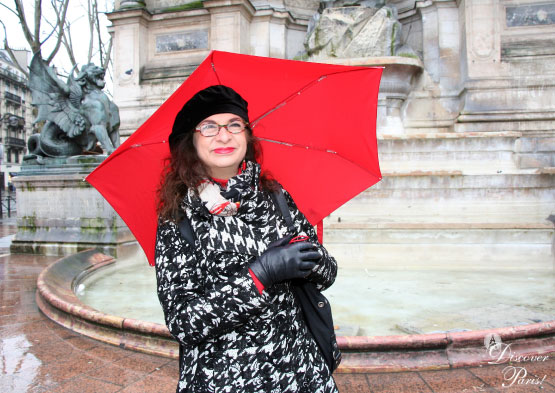 Adrian Leeds under her red umbrella in the rain next to a fountain