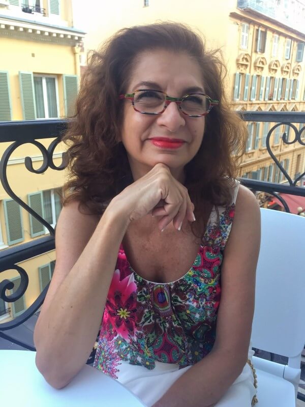 Adrian Leeds in a flower print dress sitting on her balcony in Nice