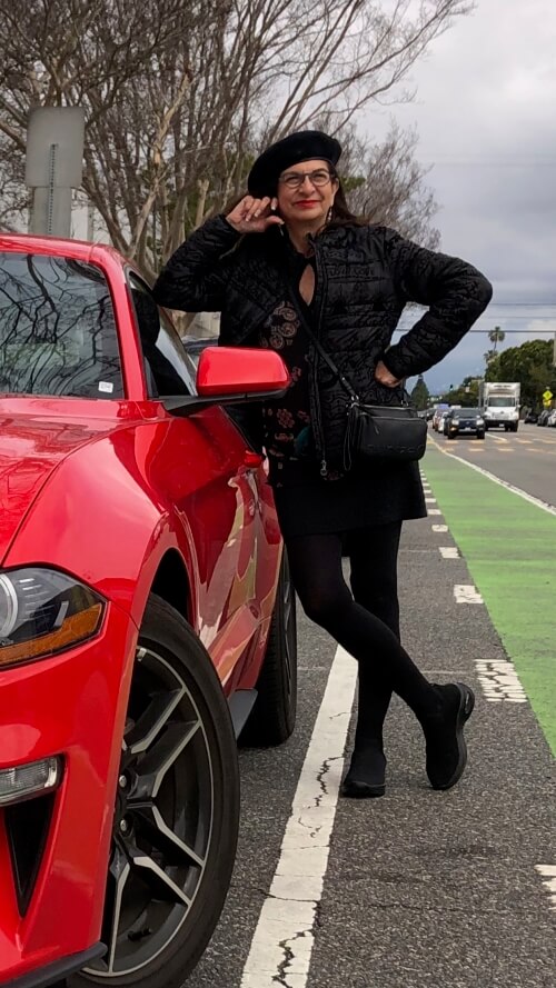 Adrian Leeds leaning on a red Mustang car in Los Angeles