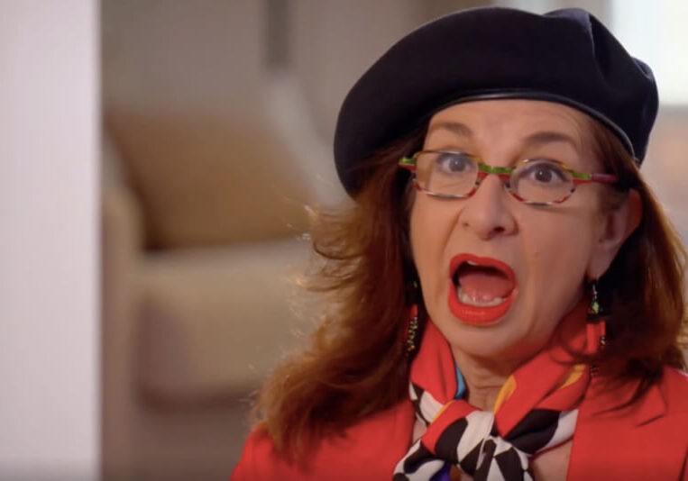 Adrian Leeds, mouth agape, gobsmacked, wearing her signature beret and a red jacket