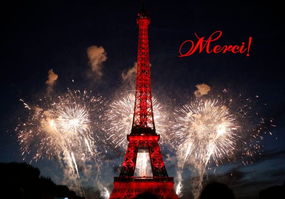 The Eiffel Tower lit in red with white fireworks going off around it