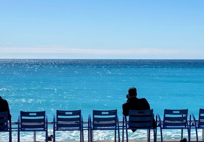 People sitting in the chaises bleu along the beach in Nice, France