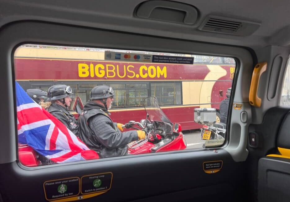 Men on motorcycles passing a taxi and a bud emblazened with BIGBUS.COM on the side